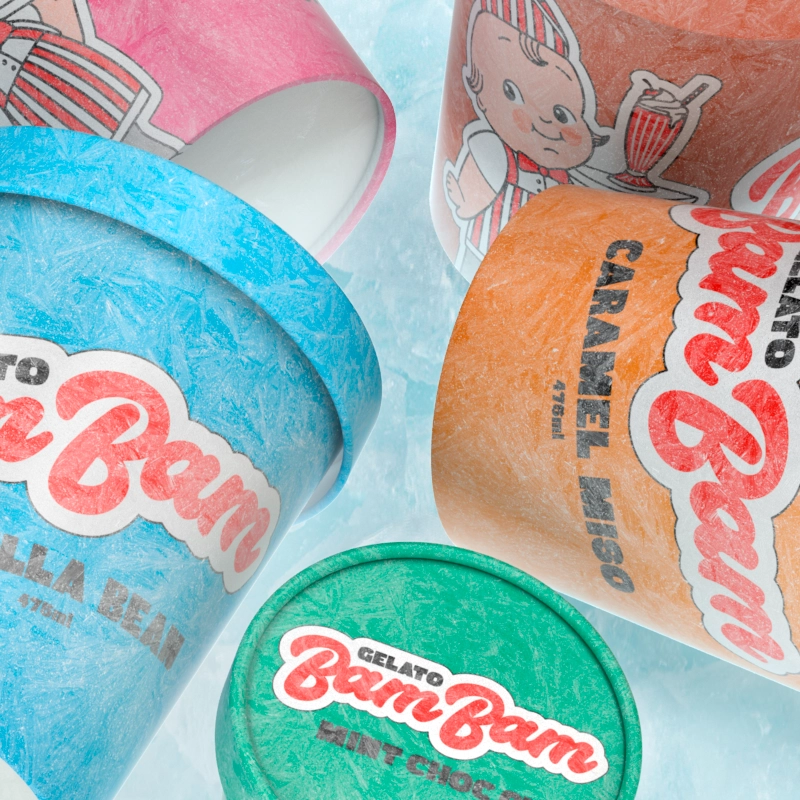 Closeup of four small tubs of Bam Bam Gelato in different colours with various flavours, sitting on a bed of ice.