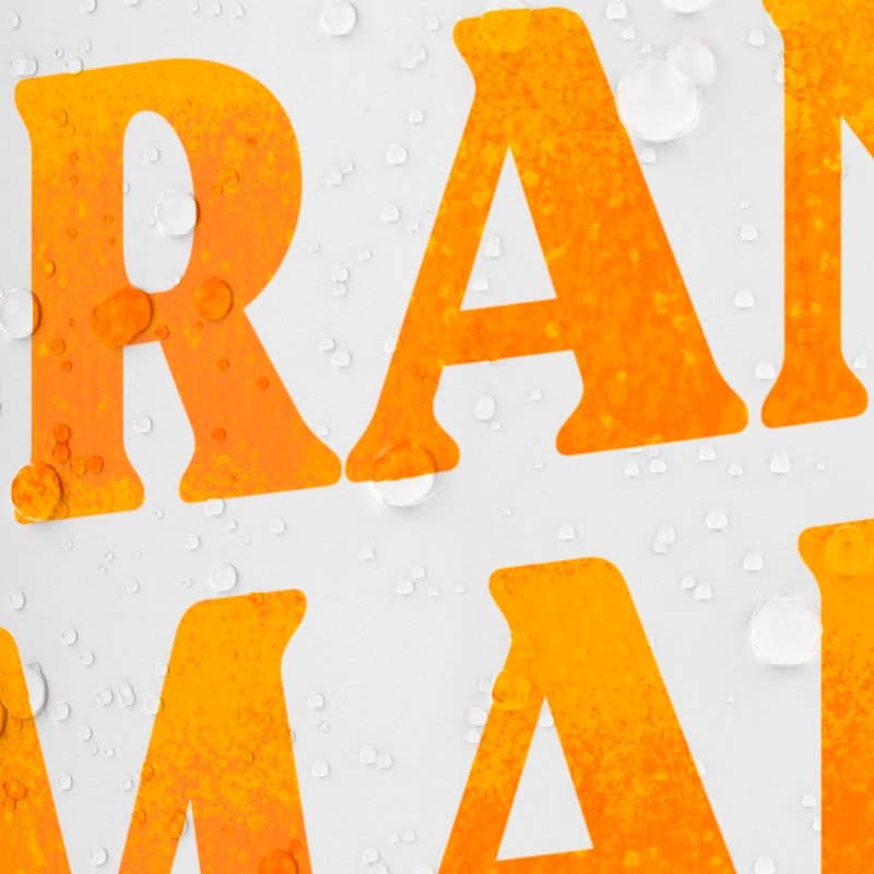 A close-up of the word "ORANGE" printed on a white surface with water droplets.