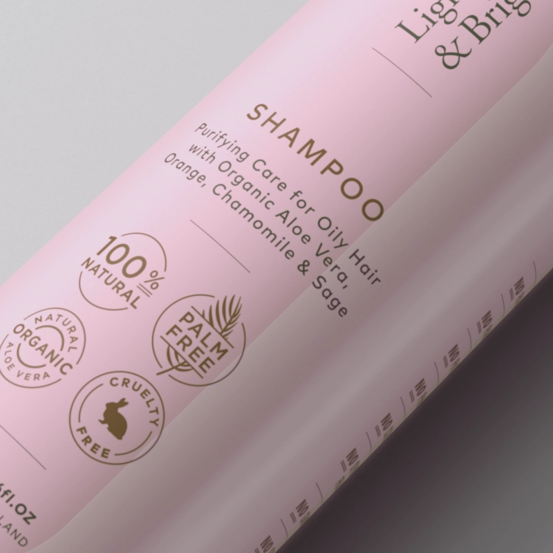 A close-up of a shampoo bottle with a pink background and gold text, highlighting its natural and cruelty-free ingredients.