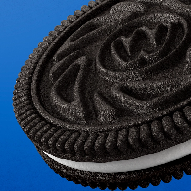 A close-up of an Oreo style (Wheelies) biscuit with a dark chocolate cookie and a white cream filling, against a blue background.